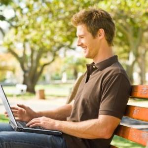 一个拿着笔记本电脑坐在公园长椅上的男人