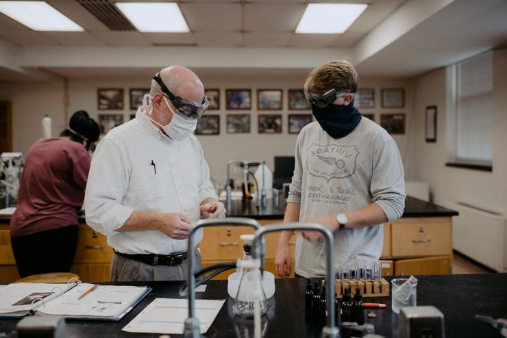 A professor and an Asbury student both in face masks work on a science experiment in a classroom laboratory