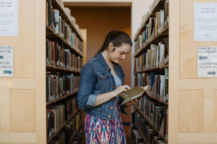 一名女学生在立博体育登录图书馆的一排书中间看书