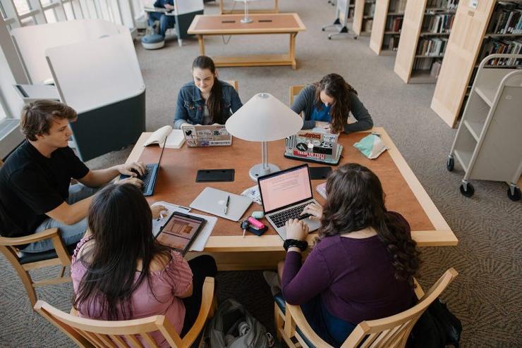 五名立博体育登录的学生围坐在图书馆的桌子旁，拿出笔记本电脑